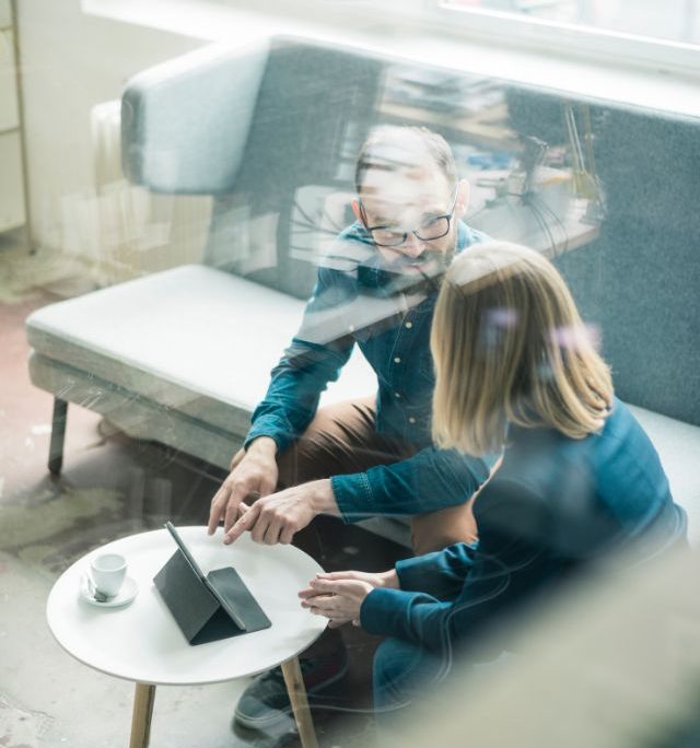man and woman sitting and discussing business mater with tablet on the table front of them 