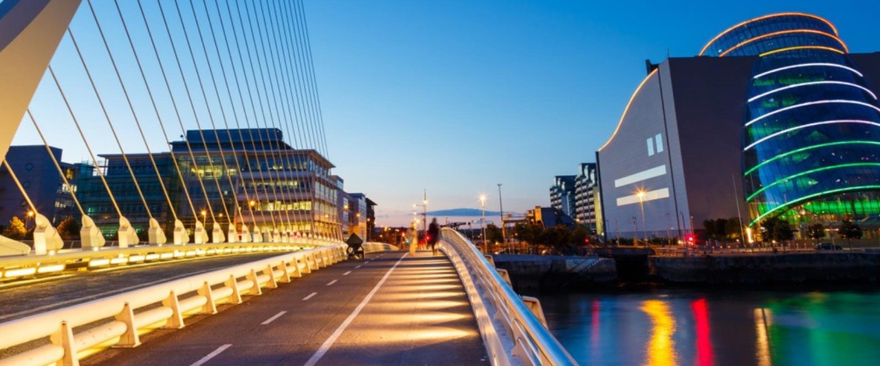 View of the iconic Samuel Beckett Bridge in Dublin at dusk, featuring modern architecture, city lights, and the River Liffey.