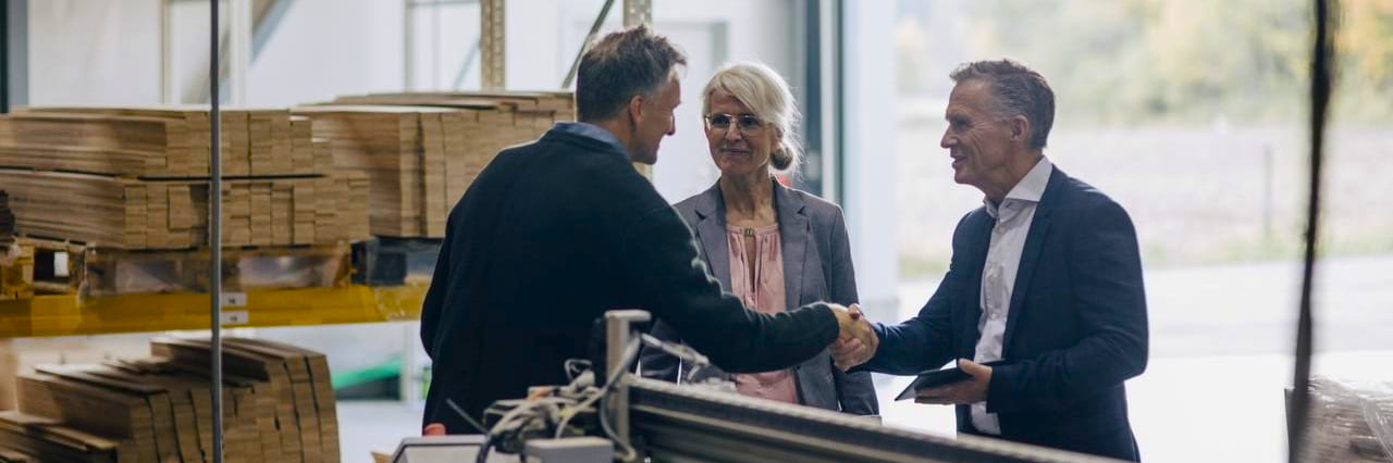 Three people discussing cooperation and shaking hands in warehouse