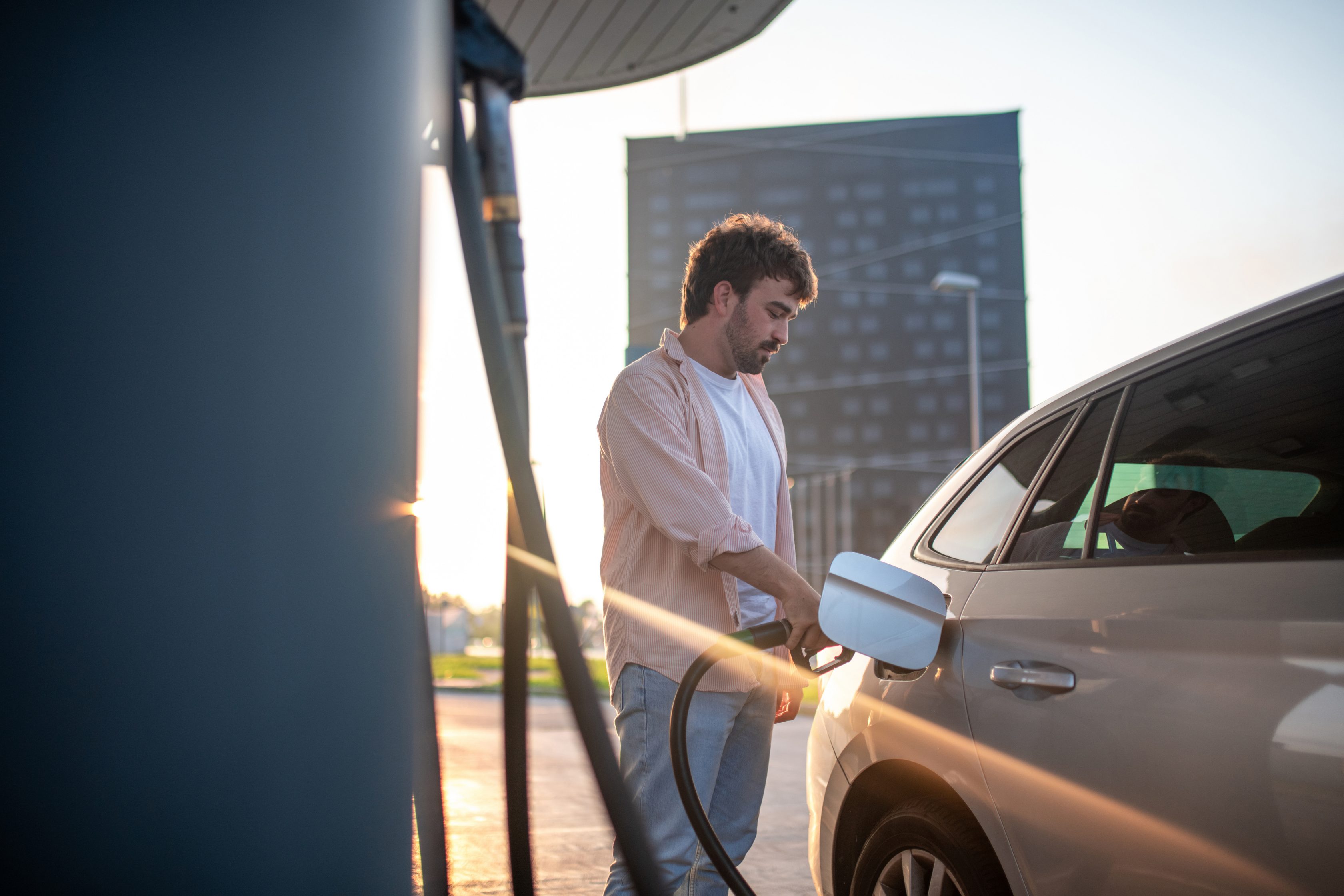 man pumping gas at gas station as the sun is setting