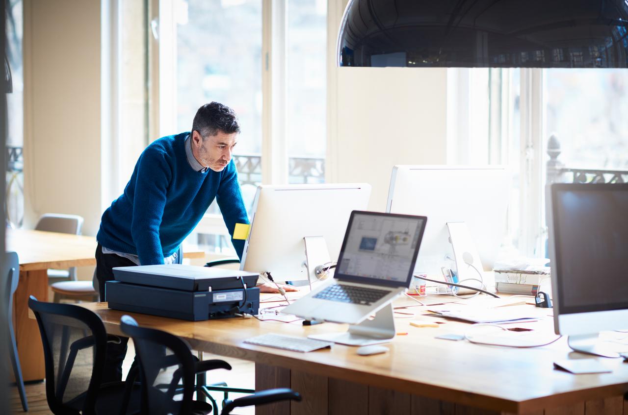 man leaning over table and looking at computer