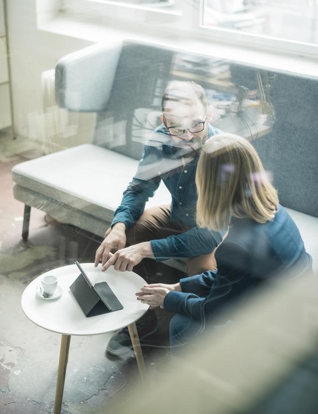 man and woman talking in office setting with tablet in front of them on table