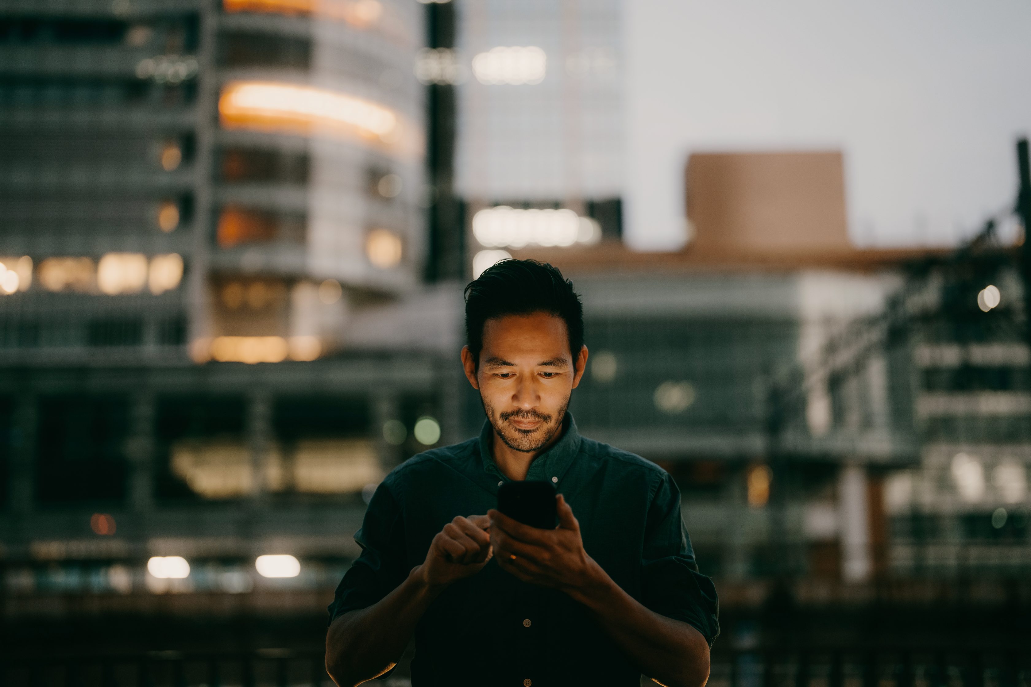 man looking down at his cell phone during nighttime