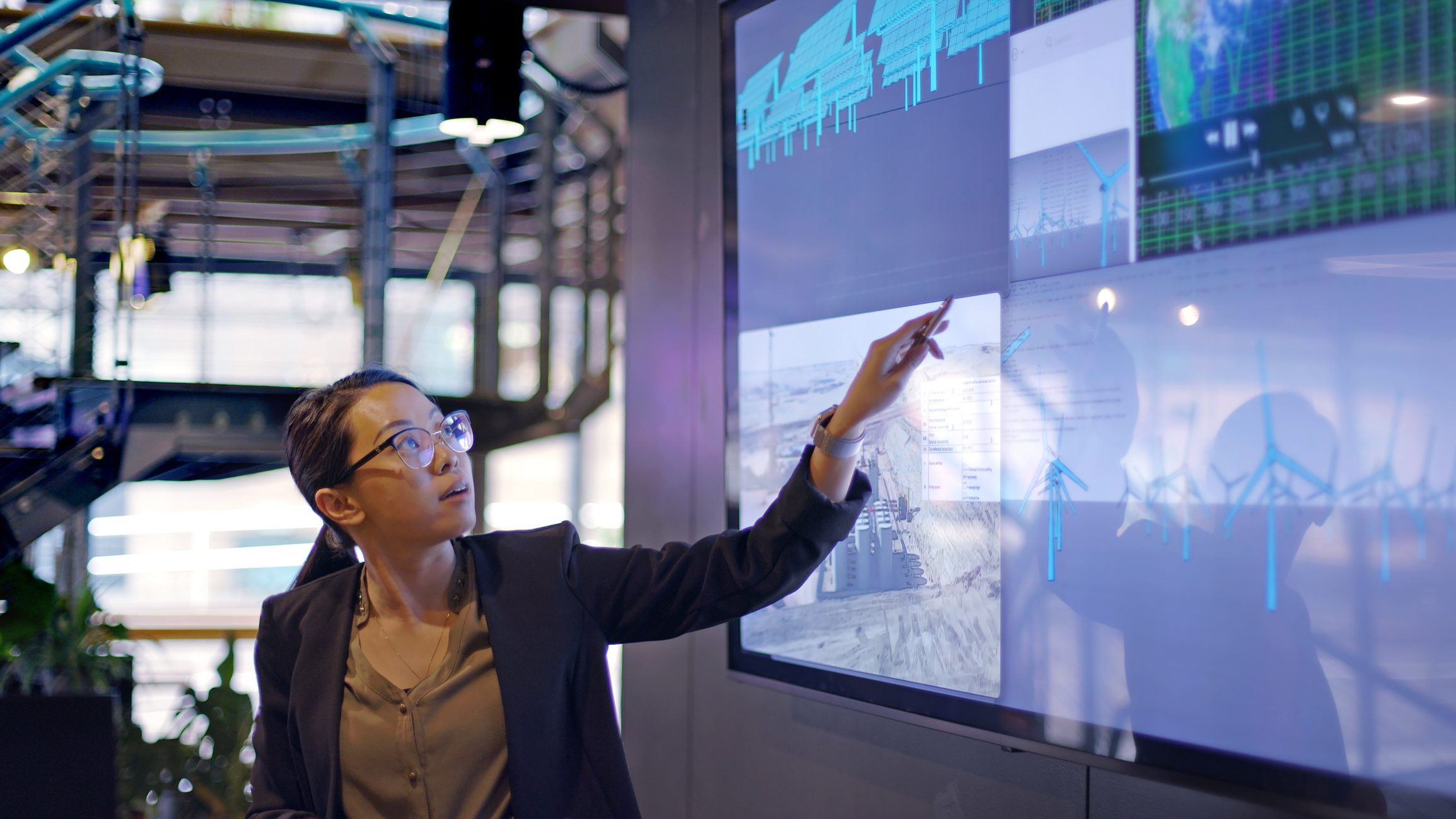 woman with glasses pointing at large screen