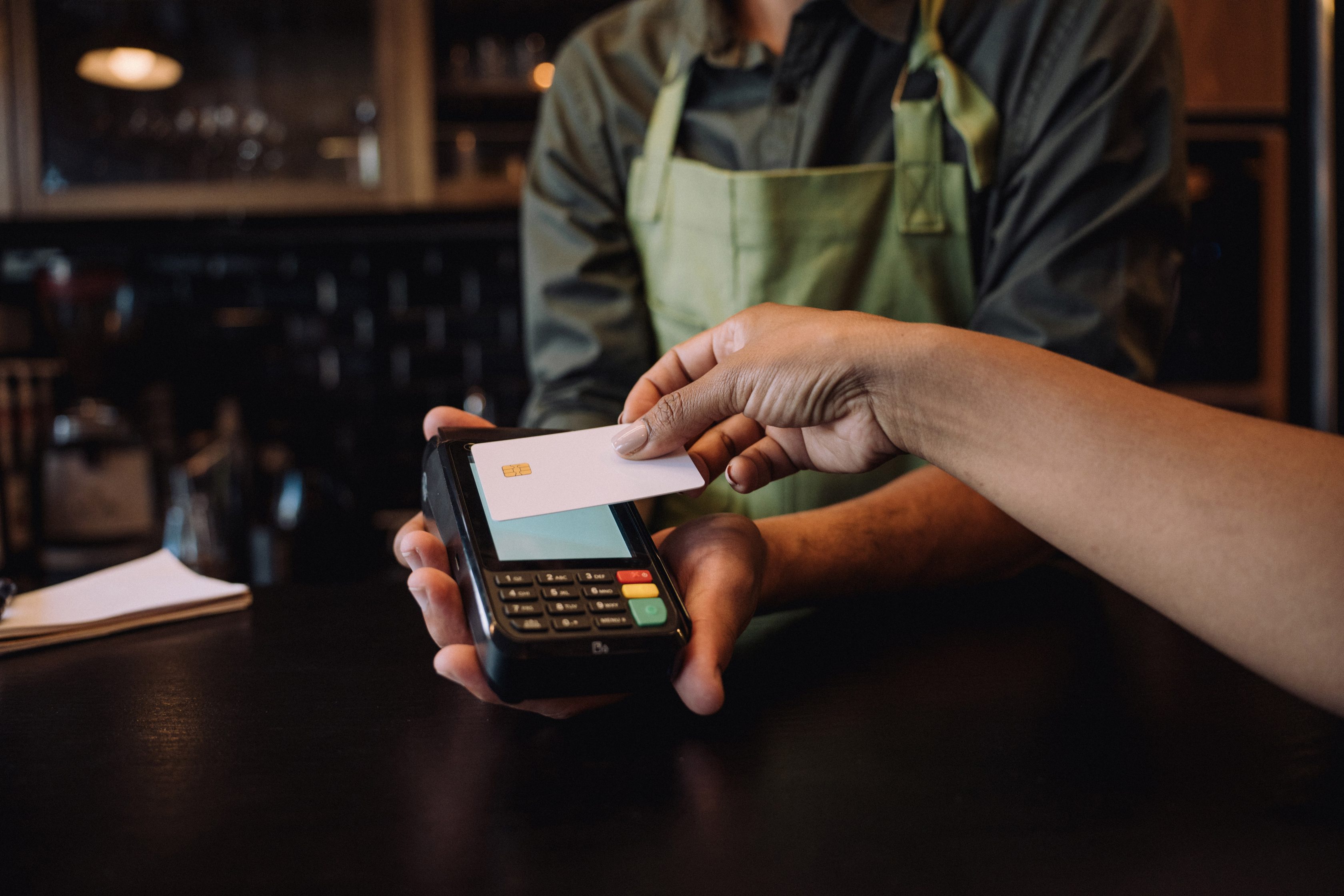caucasian arm tapping a credit card at POS system with store clerk in background