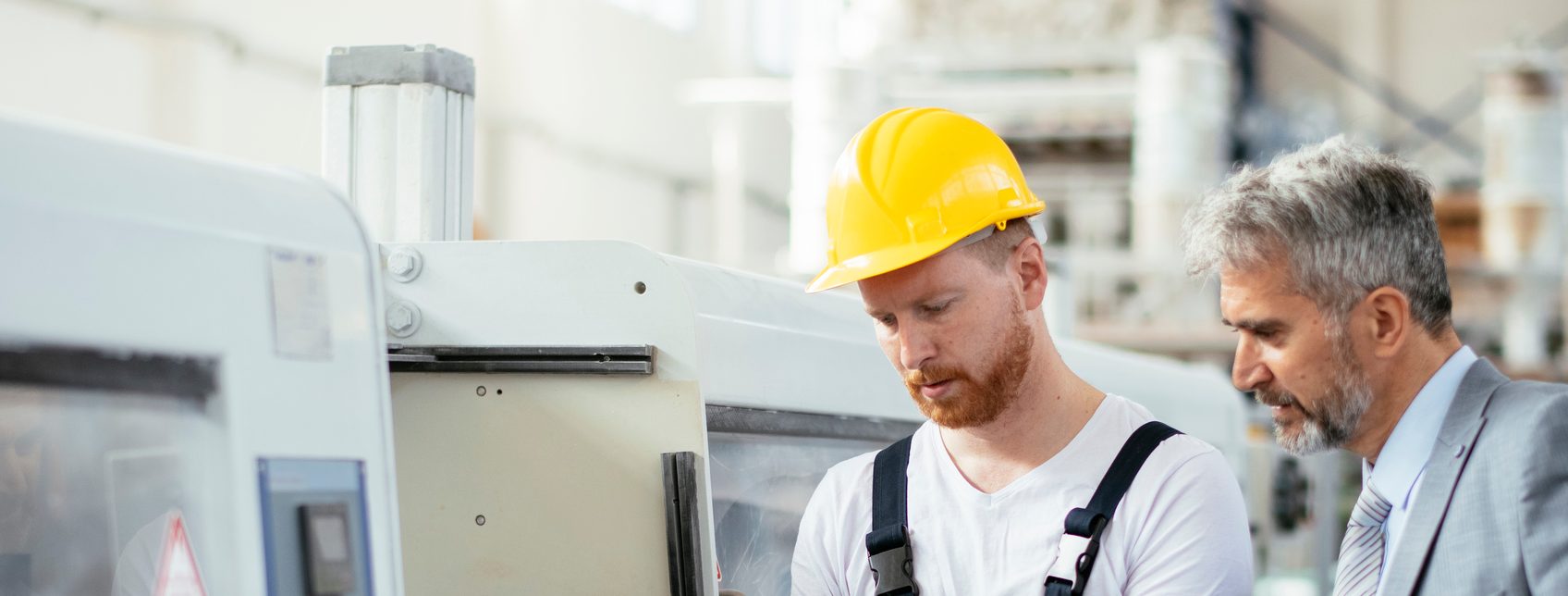 man with yellow hard hat on showing man in suit a tablet