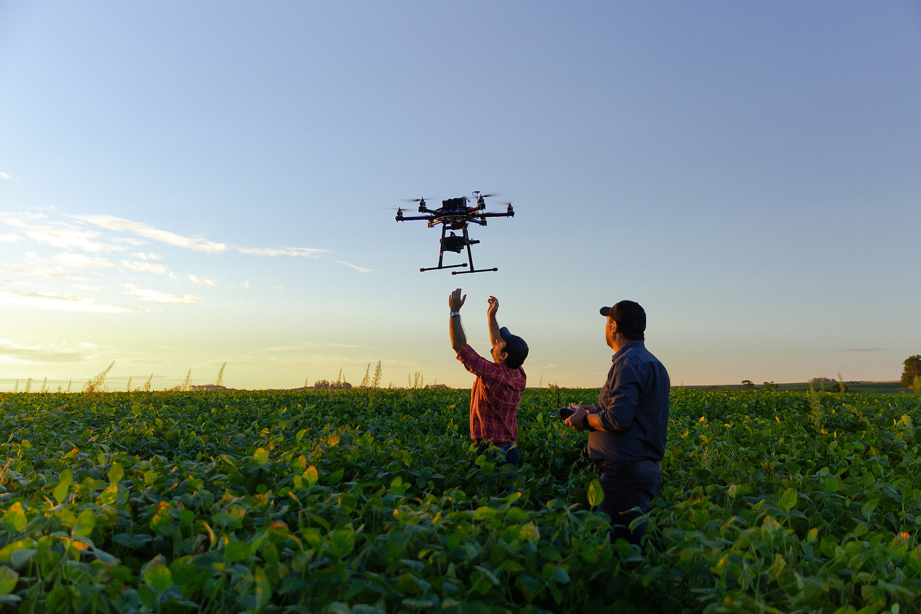 two men in field with drone being launched