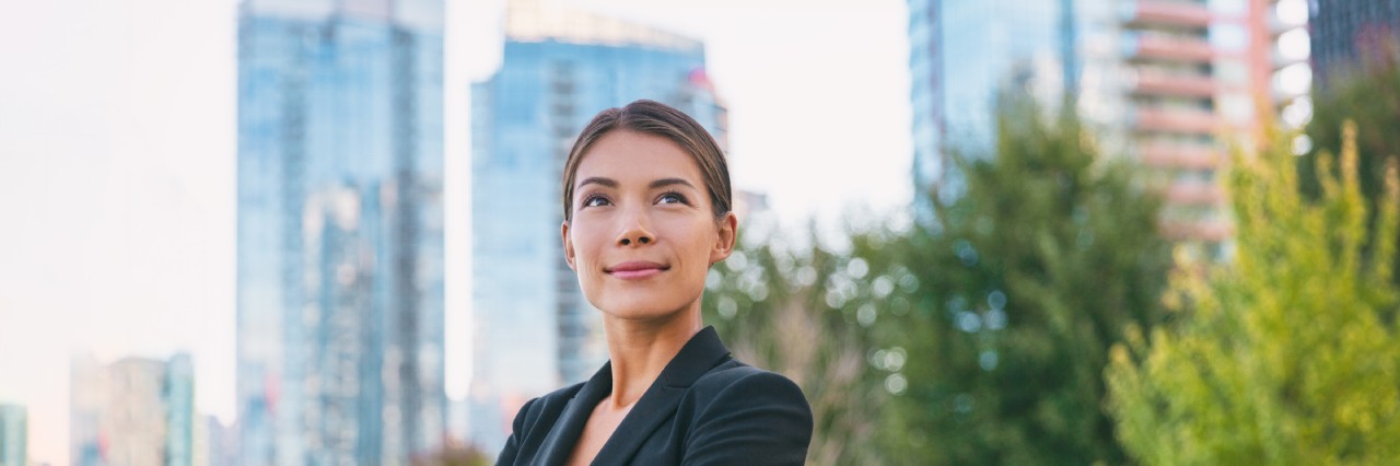 a woman standing in front of buildings facing towards the camera gazing upwards.