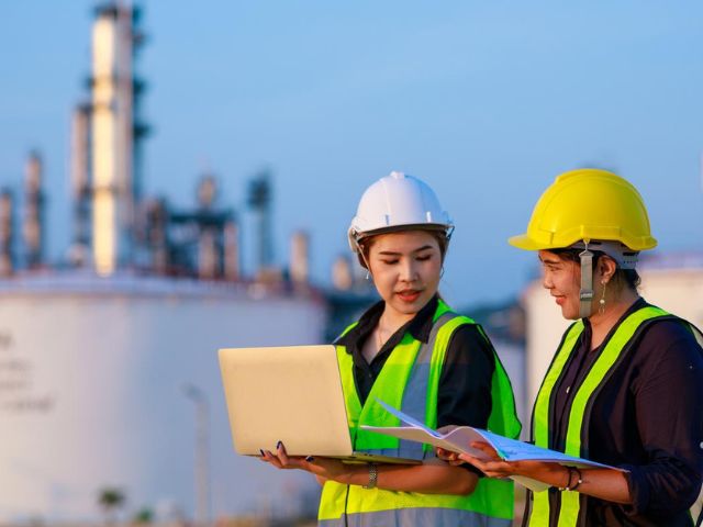 Due lavoratrici con gilet e caschi protettivi controllano i dati di un impianto di produzione