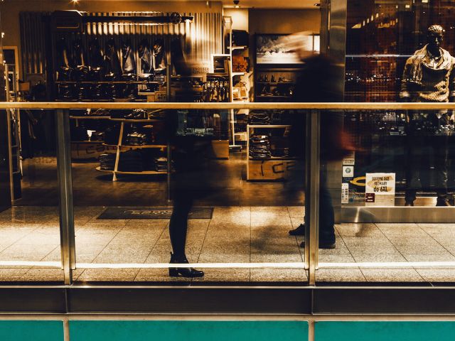 Due persone passano davanti alla vetrina di un negozio di abbigliamento maschile in un centro commerciale