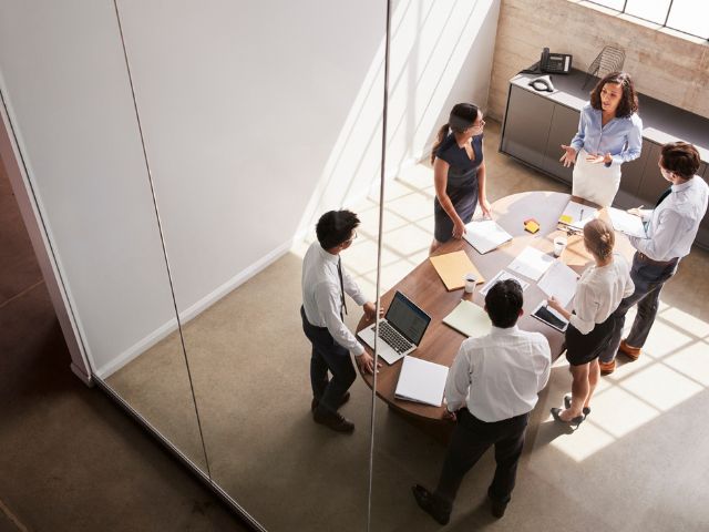 Sei colleghi in una sala riunioni in piedi intorno al tavolo
