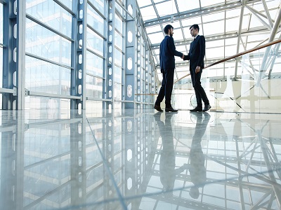 Due imprenditori si stringono la mano all'interno di un edificio con grandi vetrate