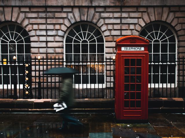 Una persona cammina con un ombrello aperto in una strada di Londra dove è presente una cabina telefonica rossa
