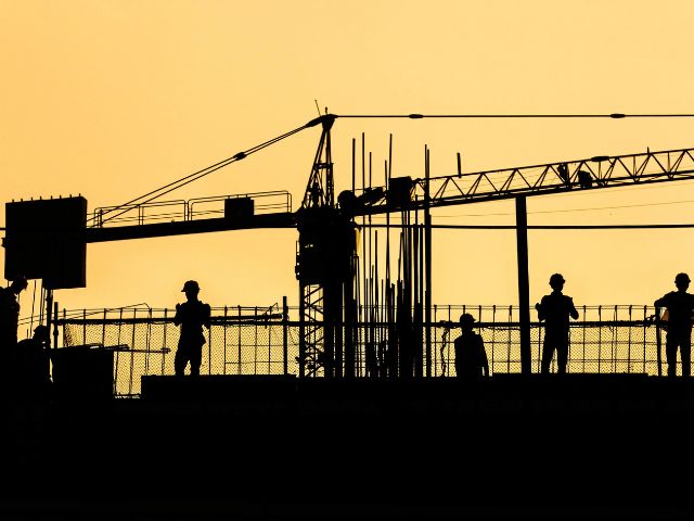 Gru e operai in un cantiere al tramonto