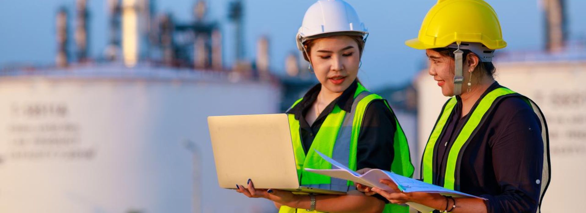 Due ispettrici con casco protettivo e gilet giallo controllano i dati di un impianto industriali