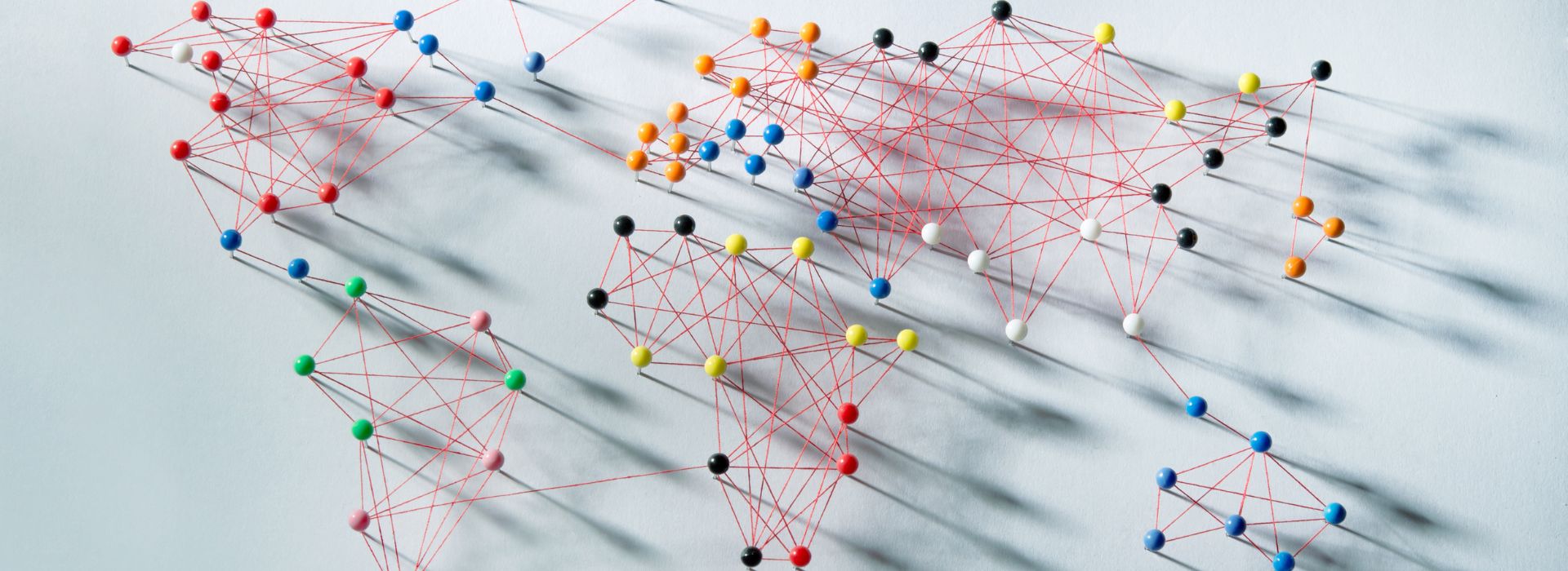 Rappresentazione dei continenti creata con puntine colorate e fili rossi tesi