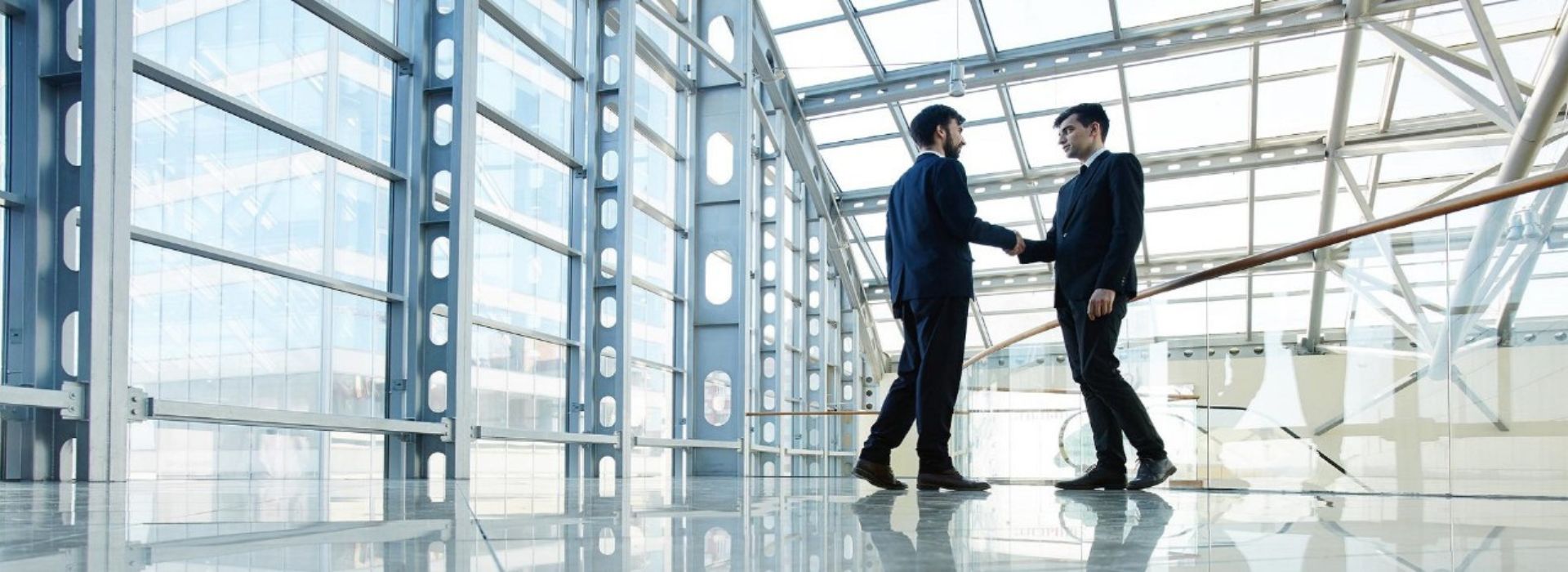 Due imprenditori si stringono la mano in un ufficio con vetrate