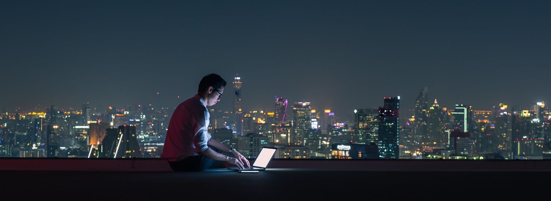 Un imprenditore lavora con il computer portatile sul tetto di un edificio con vista sulla città