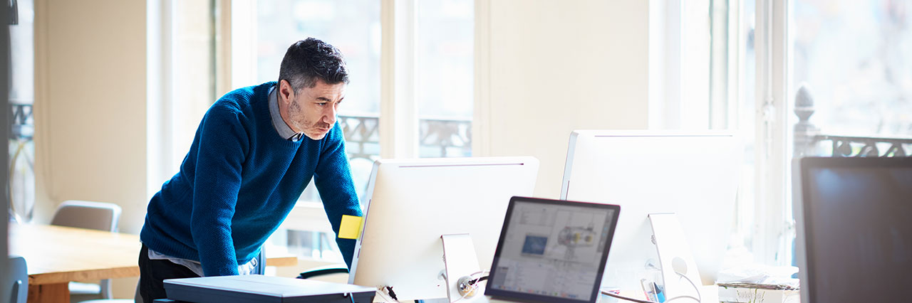 Ein mann steht vor einem Schreibtisch und blickt angestrengt auf den Computer Monitor