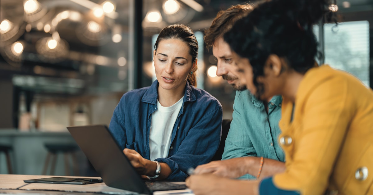 Trois personnes qui discutent autour d'une table, face à un ordinateur